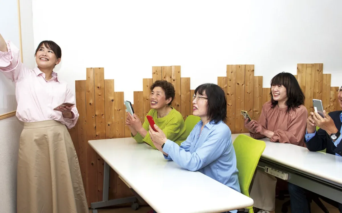 講師と数名の生徒が、スマートフォンを見ながら笑顔で学んでいる授業風景